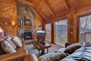 A log cabin interior with a stone fireplace, leather furniture, and a television. - Bearly Heaven (Gatlinburg)