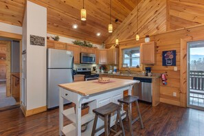 A wooden cabin kitchen with a central island, wooden cabinets, a refrigerator, microwave, and a sink. - Bearly Heaven (Gatlinburg)
