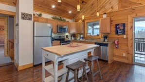 Cocina de cabaña de madera con una isla central, armarios de madera, un refrigerador, microondas y un fregadero.