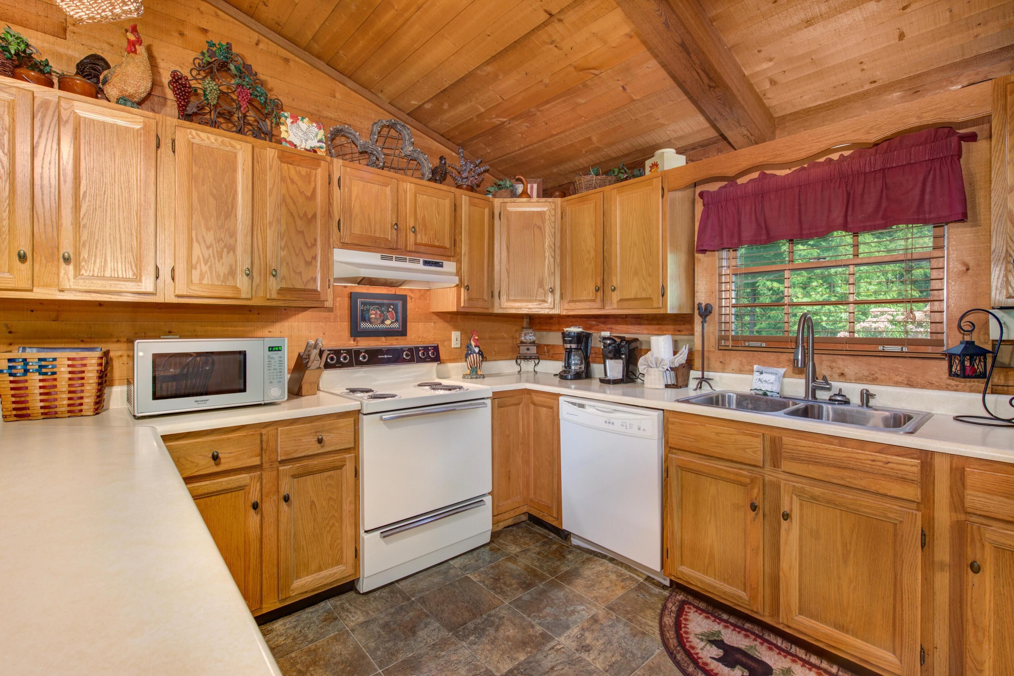 A kitchen with wooden cabinets, a microwave, stove, dishwasher, and a window with a view of greenery.