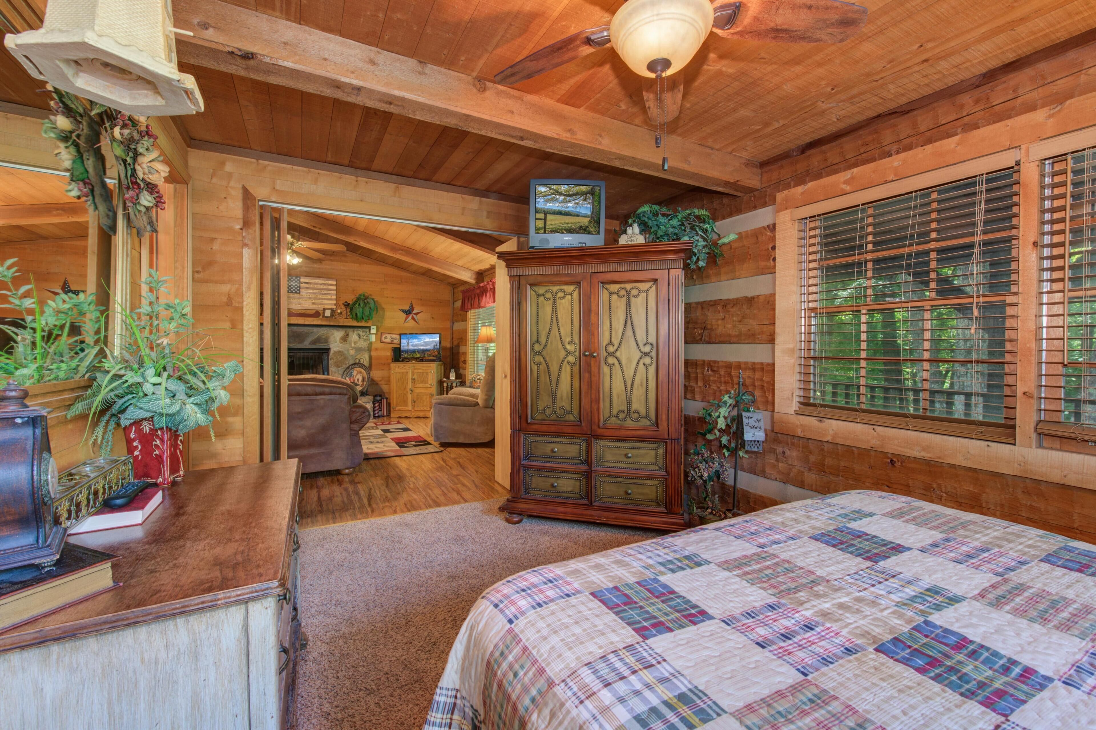 A wooden cabin interior with a bed, wooden cabinets, a fireplace, and a television.