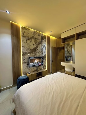 Una habitación de hotel moderna con una cama grande, un televisor montado en una pared de mármol, un escritorio con una silla y un armario.