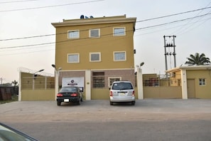 A two-story building with a gated entrance, two cars parked in front, and a clear sky.