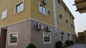 Un edificio de varios pisos con aires acondicionados, ventanas y una entrada protegida por una reja.