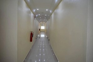 Een lange, smalle gang met een brandblusser aan de linkerwand, een betegelde vloer en in het plafond ingebouwde verlichting.