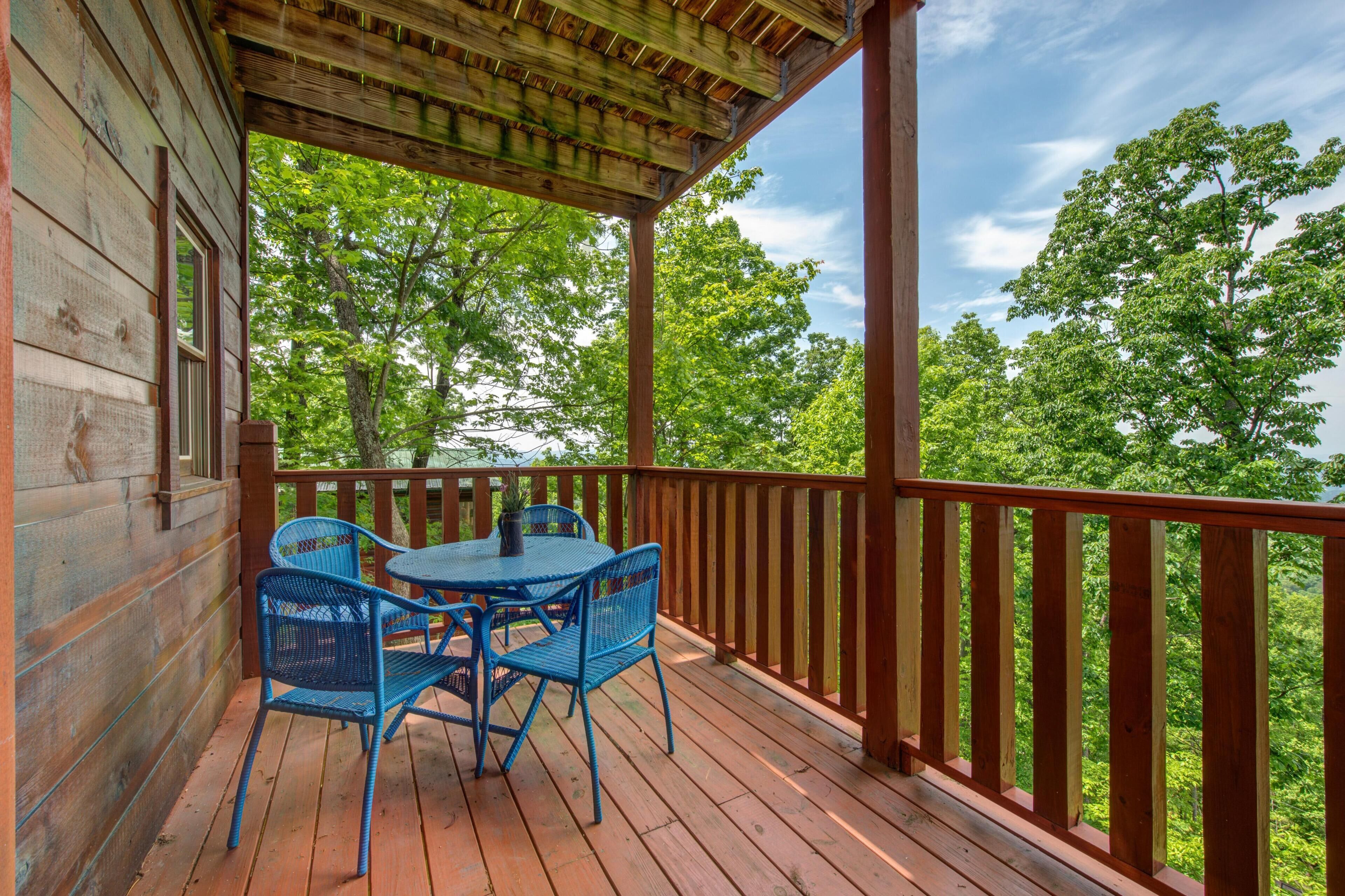A wooden deck with a table and chairs, surrounded by a wooden railing, overlooking a forested area.