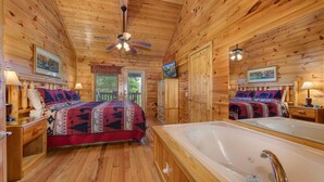 Ein Holzblockhaus-Innenraum mit Bett, einer großen Badewanne, Holzböden, Deckenventilatoren und gerahmten Kunstwerken.