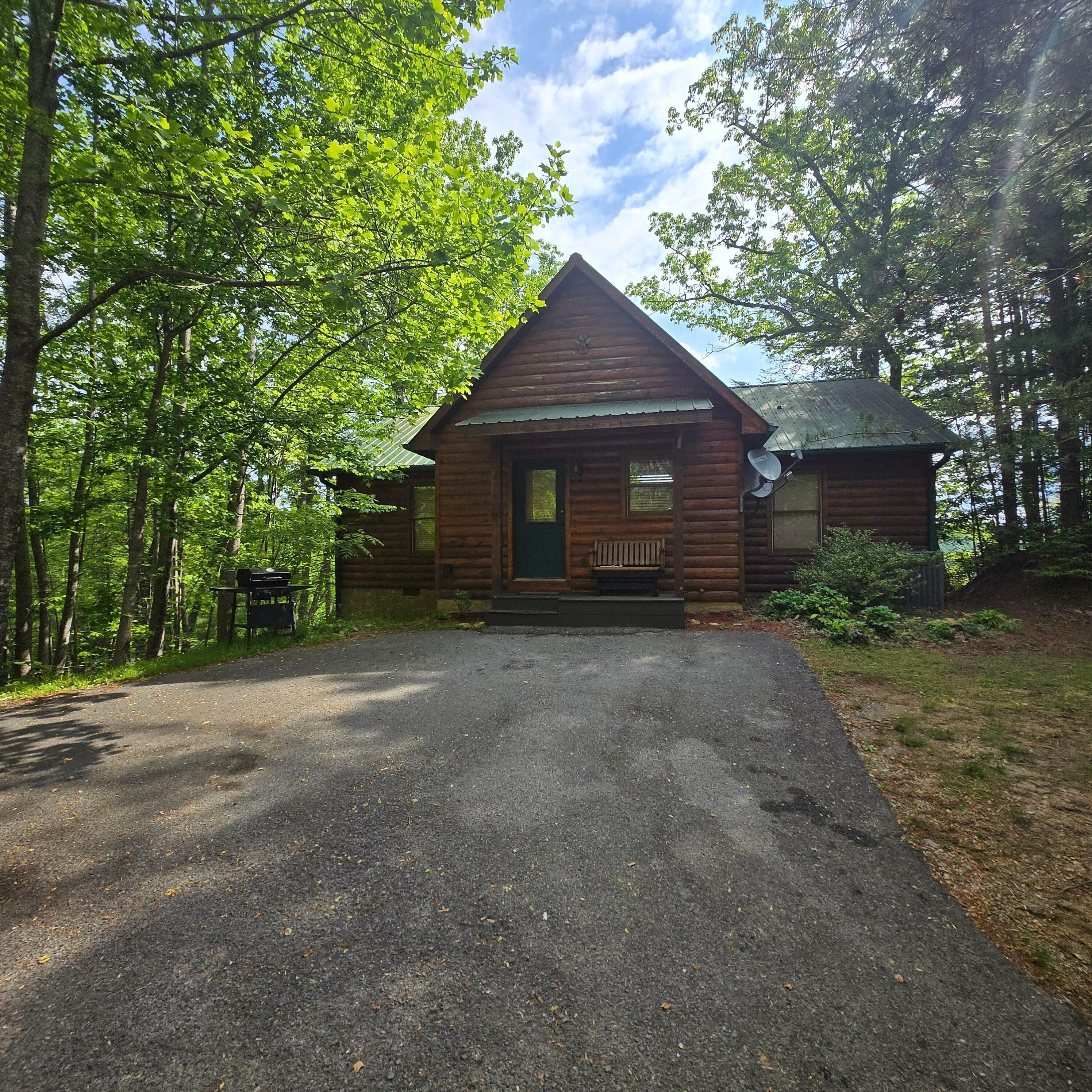 A wooden cabin with a front porch, a driveway, and a satellite dish.