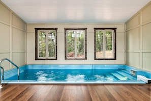 A swimming pool with wooden deck flooring, three windows with wooden frames, and a view of a forest. - Hummingbird Splash (Cosby)