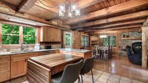 A wooden cabin interior with a kitchen, dining area, and a stone fireplace. - Eagles Perch Pool Cabin (Cosby)