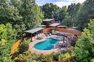Una casa de dos pisos con piscina, rodeada de un bosque frondoso.