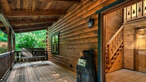A wooden cabin with a porch, a bench, a wooden sculpture, and a staircase leading to the entrance. - Eagles Perch Pool Cabin (Cosby)