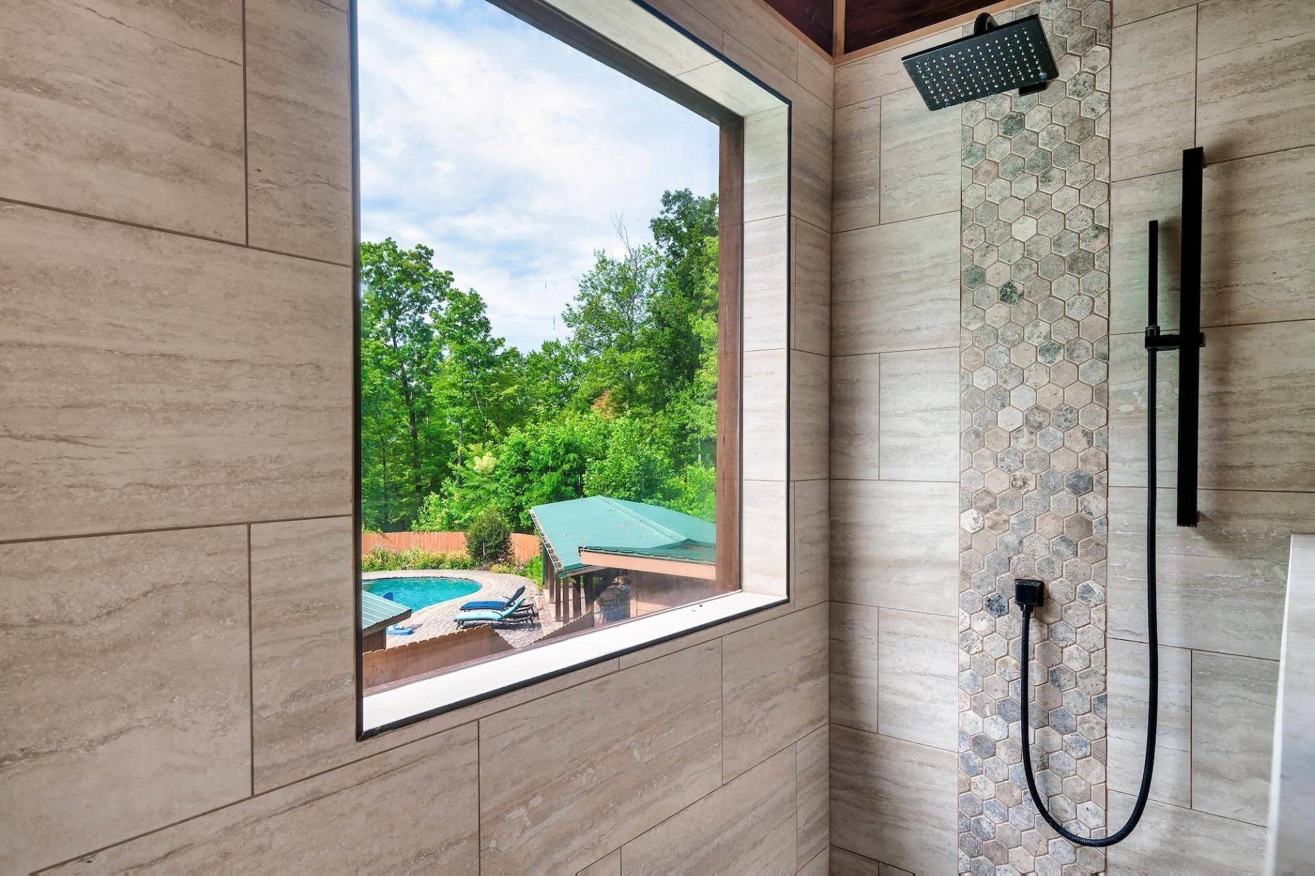 A shower with a view of a backyard, a window, and a tiled wall.