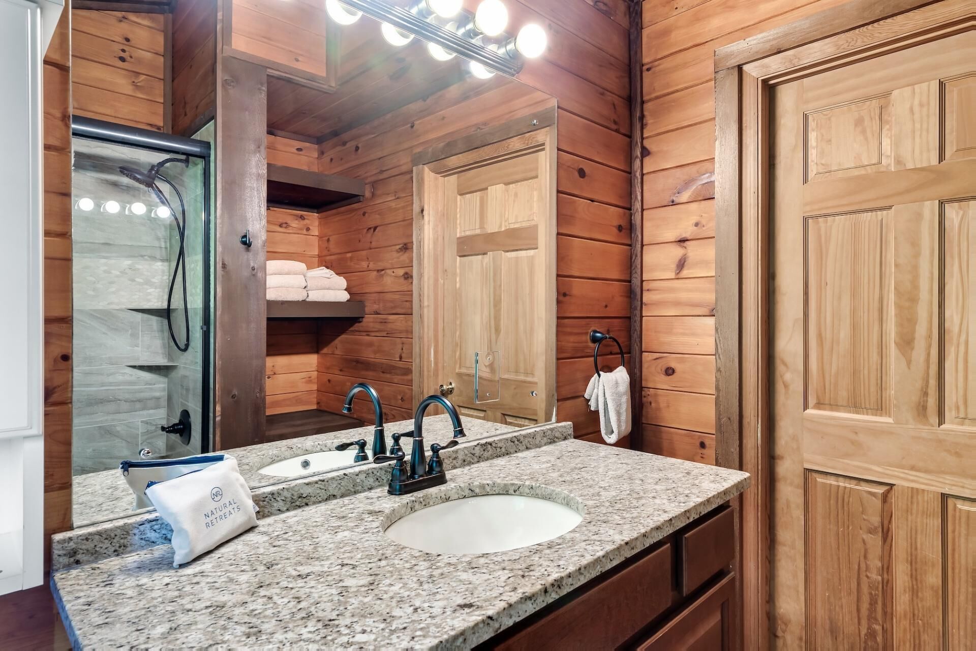 Une salle de bain de style rustique, avec des murs en bois, dotée d’un double lavabo, d’un porte-serviettes et d’un miroir.