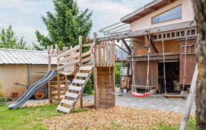 A wooden play structure with a slide and swings, set against a house with a metal roof and a window. - Apartment "Abendrot" (Freiamt)