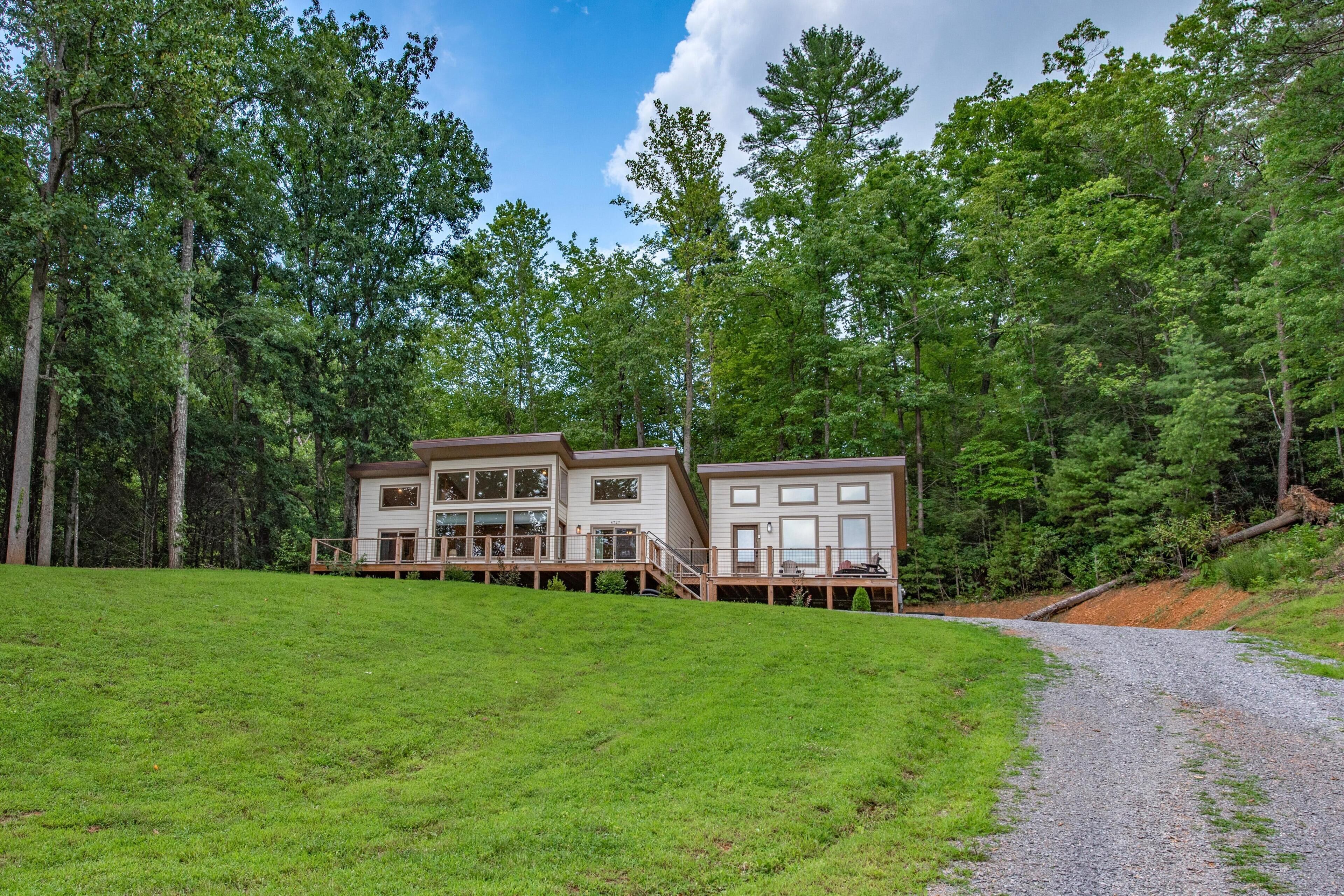 A two-story cabin with a deck, surrounded by a forest.