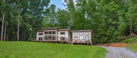 A two-story cabin with a deck, surrounded by a forest.