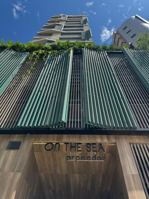 Ein modernes Gebäude mit vertikalen, grünen Lamellen, einer Holzfassade und dem Schriftzug 'ON THE SEA arpoader'.