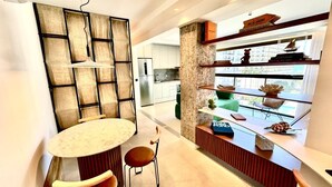 A modern kitchen with a dining area, featuring a marble countertop, a built-in bookshelf, and a view through a large window. - Luxury LOFT in Brand New 5★ Building Steps from Ipanema & Copacabana beach (Rio de Janeiro)