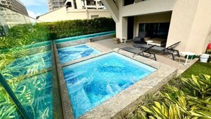 A modern outdoor pool area with two rectangular pools, surrounded by greenery and adjacent to a building with balconies. - Luxury LOFT in Brand New 5★ Building Steps from Ipanema & Copacabana beach (Rio de Janeiro)
