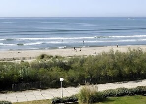 Una spiaggia con persone che passeggiano, una recinzione e una strada con un lampione.