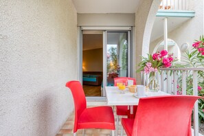 Un balcone con tavolo e sedie, una porta scorrevole in vetro e vista sull'interno.
