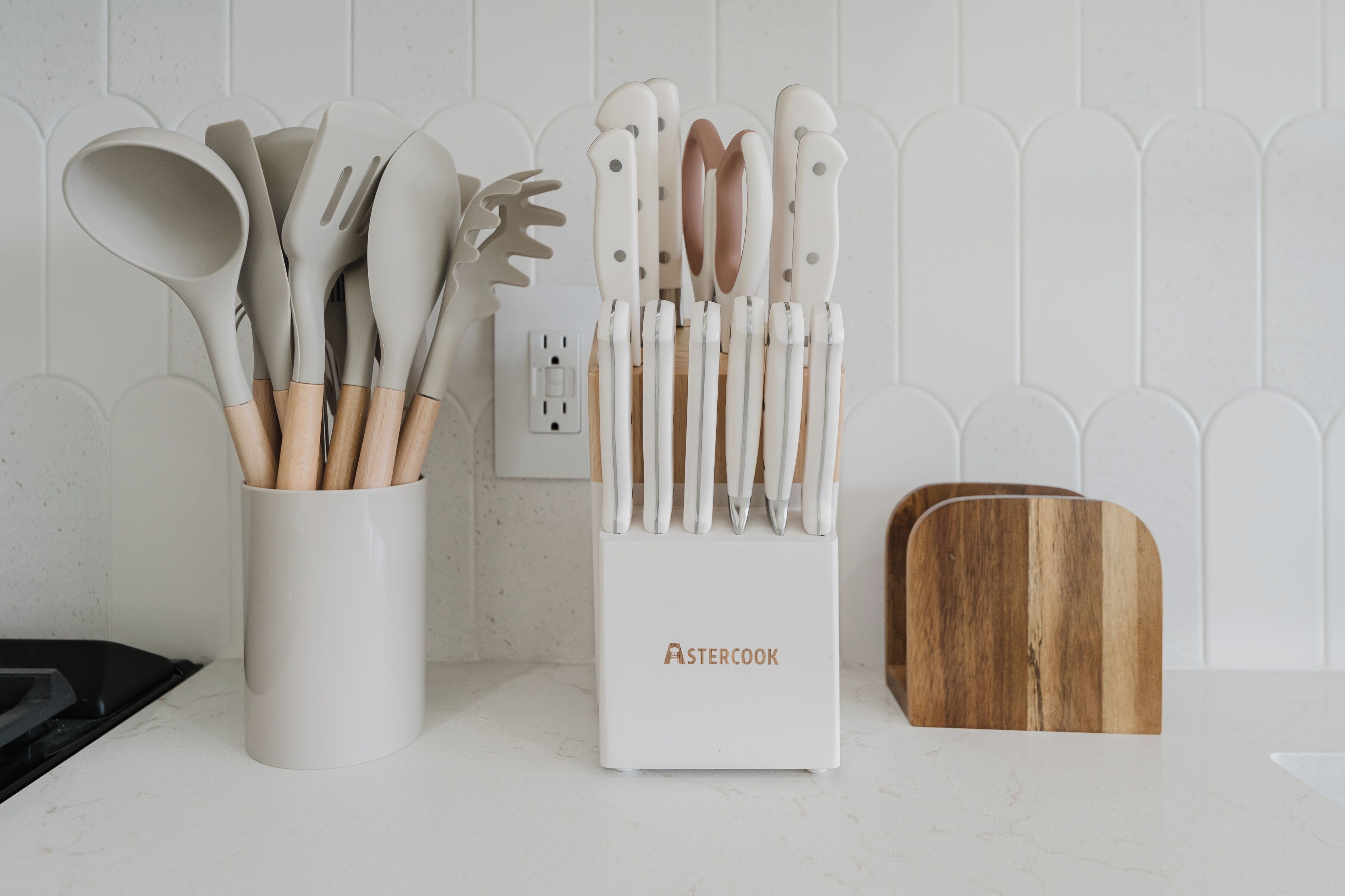 A kitchen counter with a utensil holder labeled 'ASTERCOOK' and a wooden cutting board.