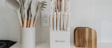 A kitchen counter with a utensil holder labeled 'ASTERCOOK' and a wooden cutting board.
