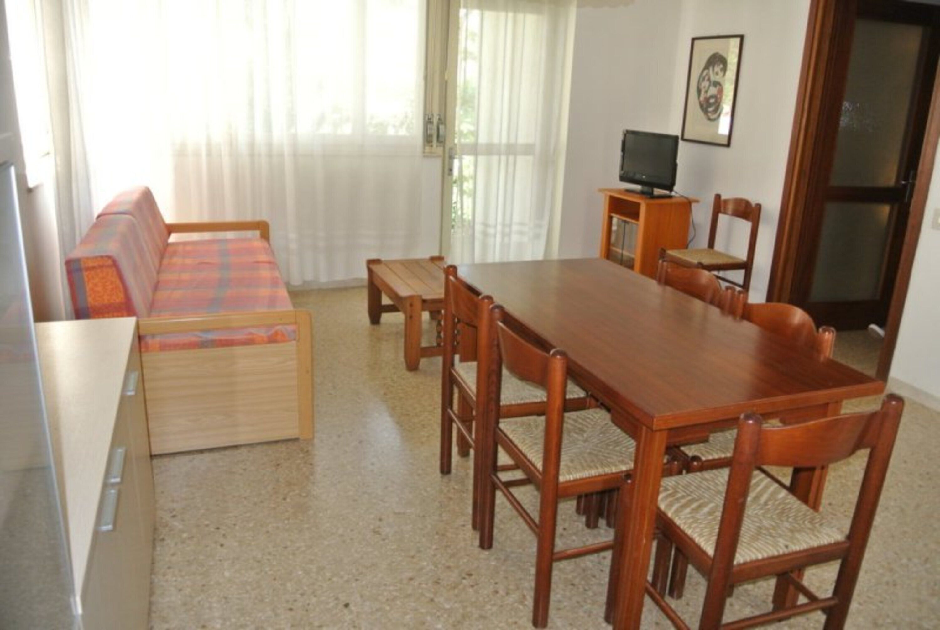 Un comedor con una mesa y sillas de madera, un sofá y un televisor sobre un mueble.