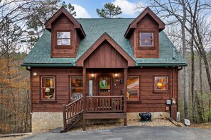 A wooden cabin with a green roof, a front porch, and a number '1547' on the door. - Whisper Ridge (Sevierville)