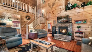A wooden interior with a fireplace, a staircase, and a living room with sofas and a coffee table. - Whisper Ridge (Sevierville)