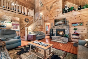 A wooden interior with a fireplace, a staircase, and a living room with sofas and a coffee table. - Whisper Ridge (Sevierville)