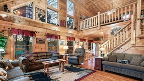 A spacious log cabin interior with a large living area, a staircase, and a view of the outdoors. - Whisper Ridge (Sevierville)