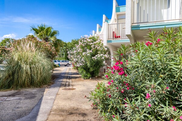 A residential street with houses, a parked car, and lush greenery. - Studio Terrace 261 by the Sea (La Grande-Motte)