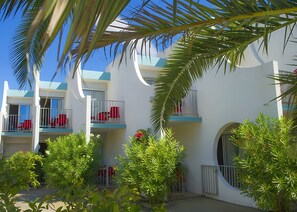Um hotel com várias varandas, cadeiras vermelhas e vegetação exuberante.