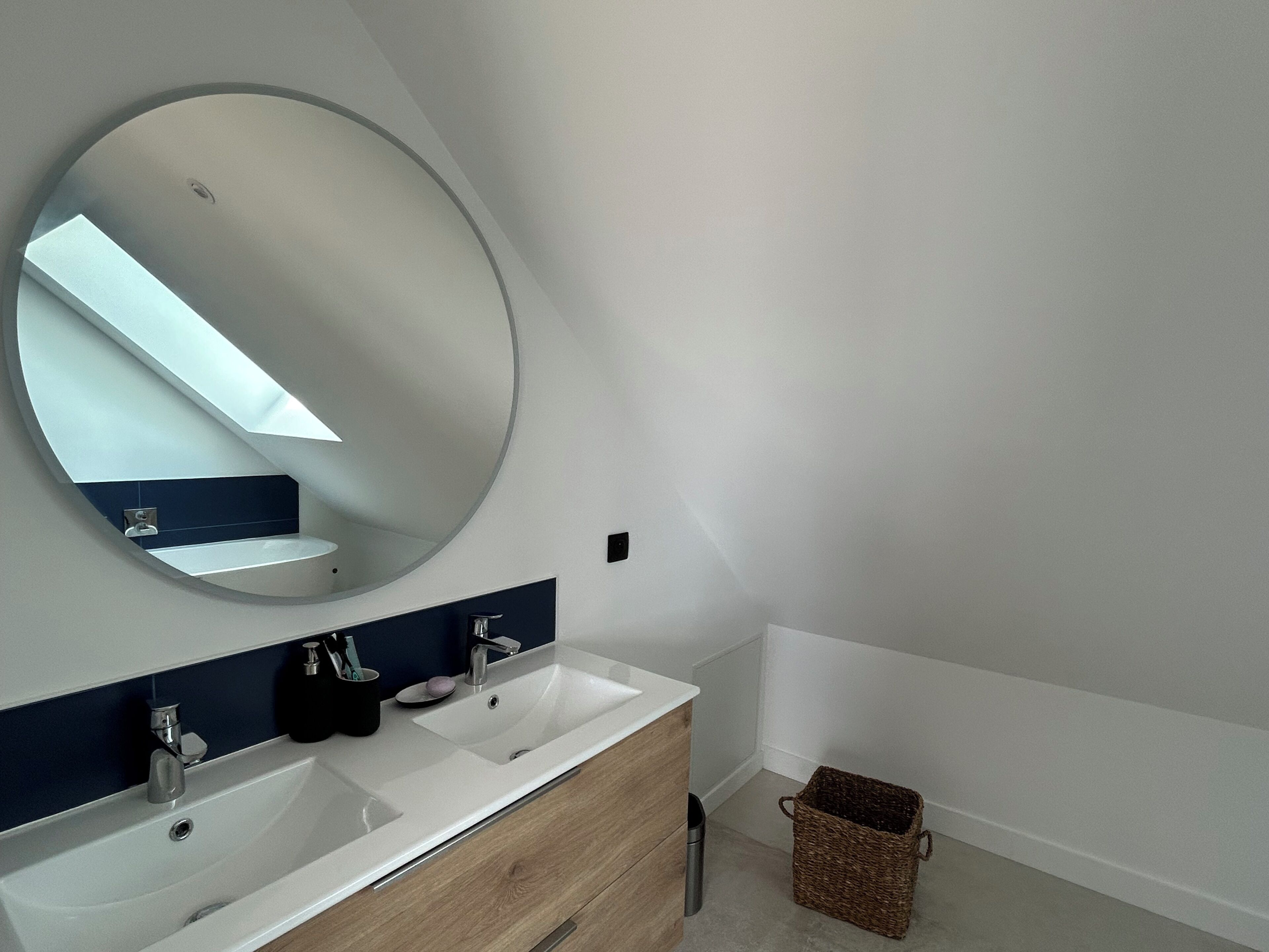 Ein modernes Badezimmer mit zwei Waschbecken, einem großen Spiegel und einem kleinen Korbwannenaufsatz.