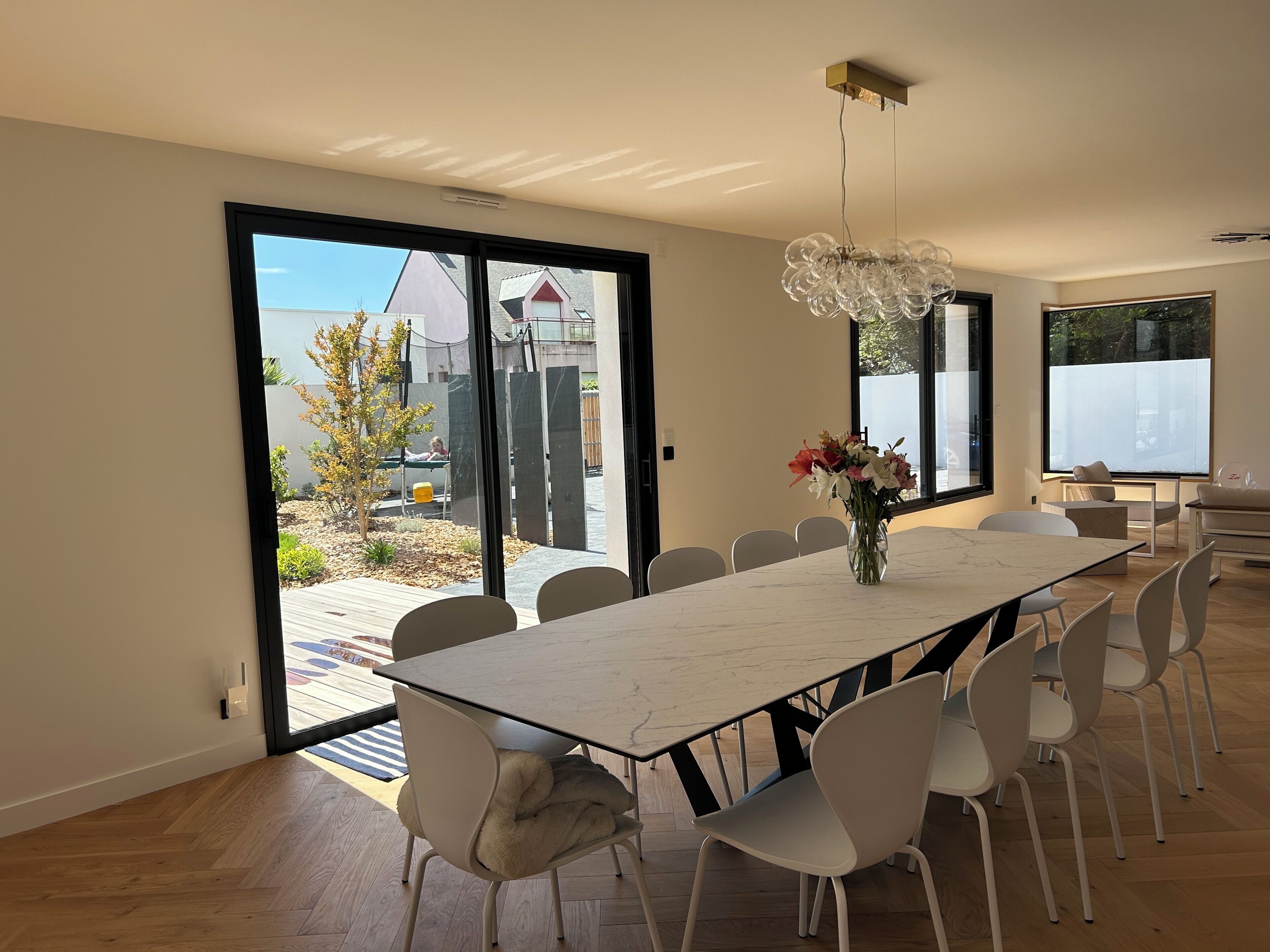 Un espace repas moderne avec une grande table, des chaises blanches et un vase de fleurs.