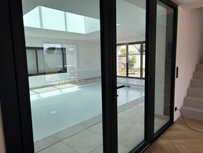 A modern interior with a glass door leading to an outdoor area with a pool and patio furniture. - Villa Zoliette (Batz-sur-Mer)