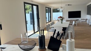 Een moderne keuken met een inbouw inductiekookplaat, een eethoek met een lange tafel en stoelen, en een groot raam met uitzicht op zee.