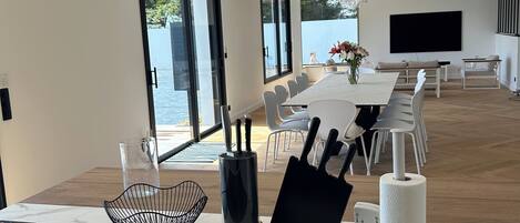 Una cucina moderna con piano cottura a induzione integrato, una zona pranzo con un tavolo lungo e sedie, e un'ampia finestra con vista sul mare.