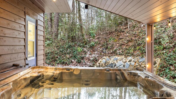 A hot tub with a stone wall backdrop, wooden siding, and a forest view. - Heavenly Sunshine (Gatlinburg)