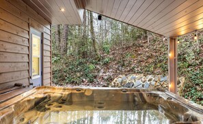 A hot tub with a stone wall backdrop, wooden siding, and a forest view. - Heavenly Sunshine (Gatlinburg)