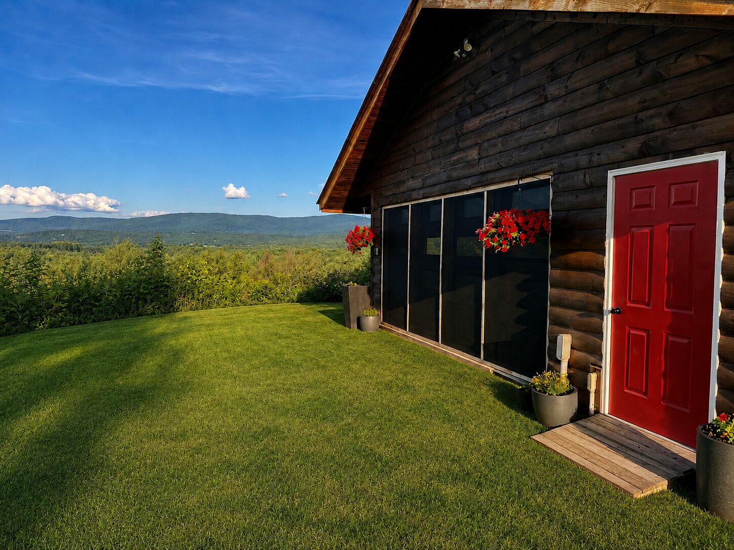 Une cabane en rondins avec une porte rouge, de grandes fenêtres et une pelouse verdoyante.