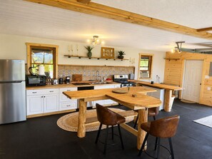 Moderni keittiö, jossa on puutasot, ruostumattomasta teräksestä valmistettu jääkaappi ja keskellä sijaitseva saareke, jonka ympärillä on jakkaroita.