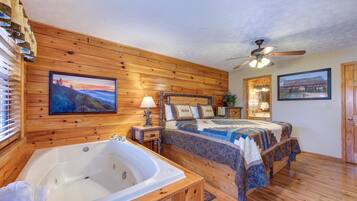 Een slaapkamer met houten lambrisering, een groot bed, een aparte badkamer met bad en een plafondventilator.