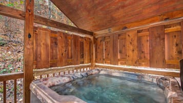 Een houten jacuzzi met een houten terras en leuningen, omringd door bomen.