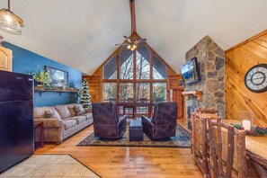 A cozy interior with a stone fireplace, a large window, and a wooden ceiling. - Playin Hookie (Sevierville)