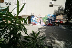 A building with a colorful mural on the wall, a paved area, and some greenery in the foreground.