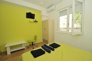 Una habitación con cama, escritorio, silla, televisor y armario.