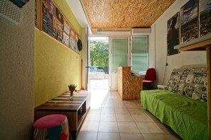 A room with a wooden ceiling, a green bed, a desk with a chair, a small table with a plant, and a bulletin board on the wall.